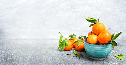 Fresh Tangerines with green leaves in blue bowl over rustic background, side view, banner