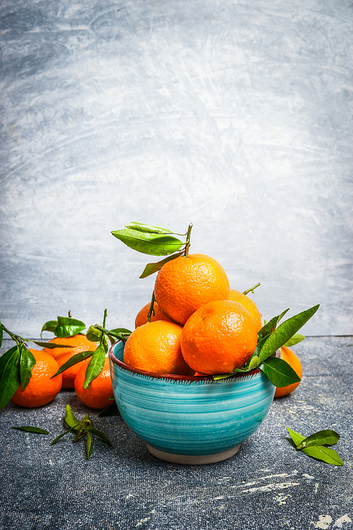 Fresh Tangerines with green leaves in blue bowl over rustic background, side view