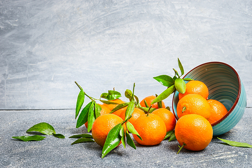 Tangerines with green leaves and bowl on rustic background, side view
