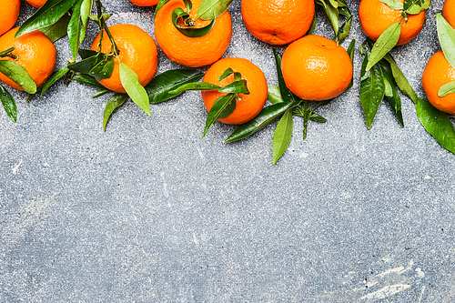 Tangerines with green leaves on rustic background, top view, border