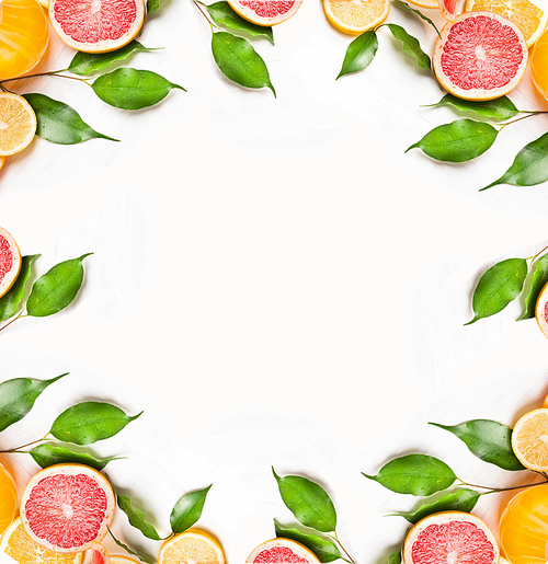 Citrus slices of orange,lemon and grapefruit with green leaves on white wooden background, frame, top view