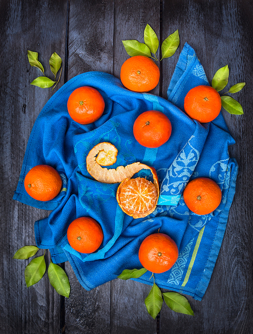 Tangerines with green leaves on  blue towel , dark wooden background, top view