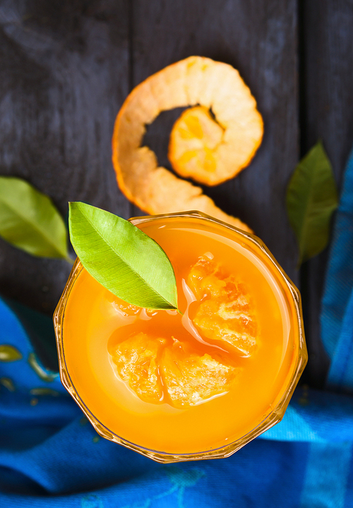 tangerine juice with green leaves in  glass on  blue wooden background , top view, close up