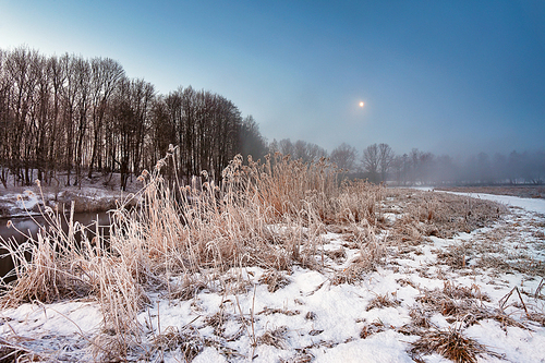 Moonlight in the winter dawn. Fog and mist on snowy winter river in Belarus.