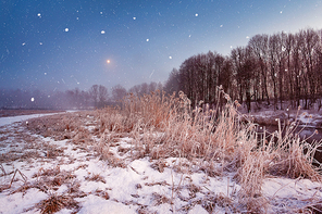 Magic winter Christmas night. Snowfall scene on a river. Frost and snowflakes under the moonlight