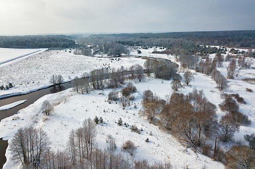 Aerial view of forest river in winter day. Winter snowy landscape with river, forest and meadow