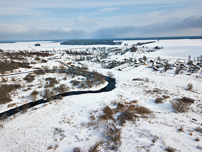 Winter rural landscape. Village and fields covered by snow. Aerial view of small river bends
