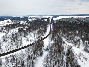 Aerial view of road bends in winter forest. Winter snowy landscape with river, forest, road and meadow