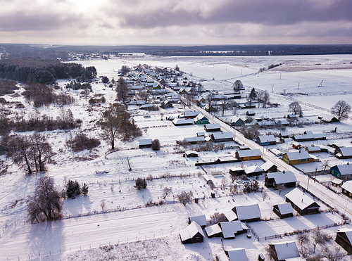 Winter rural landscape. Aerial view of village, houses, meadow and forest covered by snow. Belarus