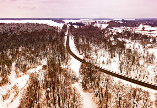 Winter snowy landscape with river, forest, road and meadow. Aerial view of road bends in winter forest.
