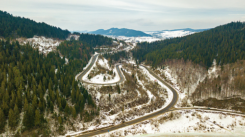 Road serpentine in winter snowy mountain landscape. Aerial rural view of road passing to horizon. Carpathian mountains, Beskids range