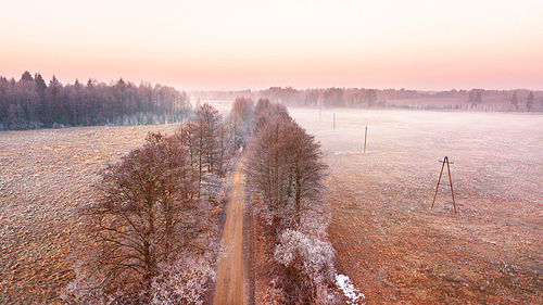 Rural misty dawn morning landscape. Aerial view of frozen road in early spring. Beautiful sunrise in Belarus.