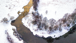 Aerial view of snowy river in winter. Frozen trees on a riverbank and meadow in Belarus near Minsk