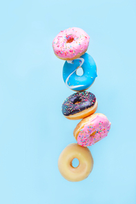flying doughnuts - balancing tower of multicolored sweet donuts with sprinkles on blue background