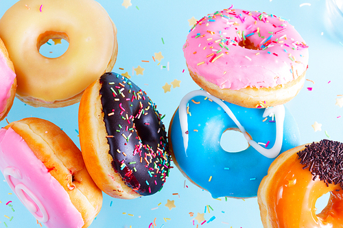 flying doughnuts scene - mix of multicolored sweet donuts with sprinkles on blue background close up