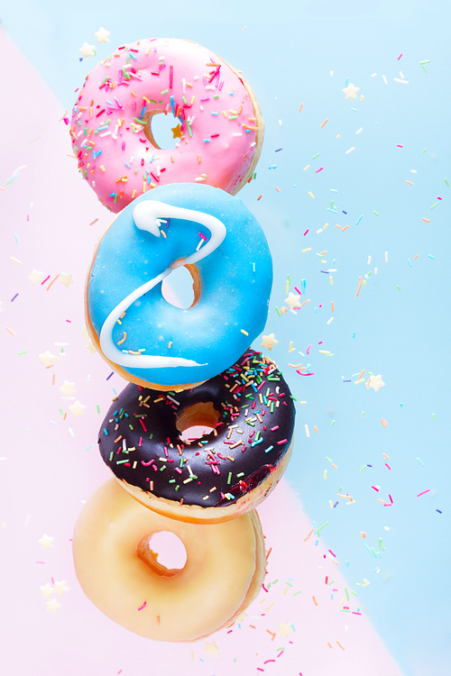 falling doughnuts chain - mix of multicolored sweet donuts with sprinkles on blue and pink background