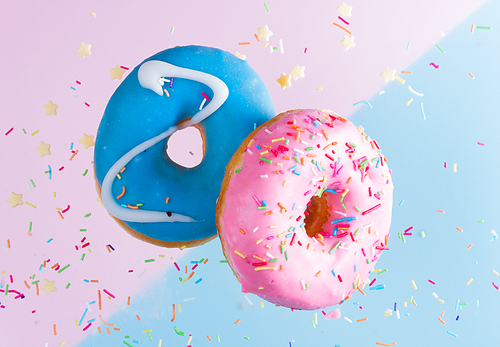 Two flying sweet doughnuts with sprinkles on blue and pink background