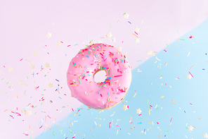 one falling sweet doughnut with sprinkles on blue and pink abstract background with copy space