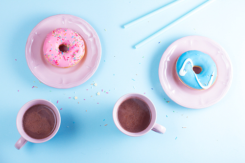 Two sweet doughnuts with two cups of cacao on blue and pink background with copy space, top view scene