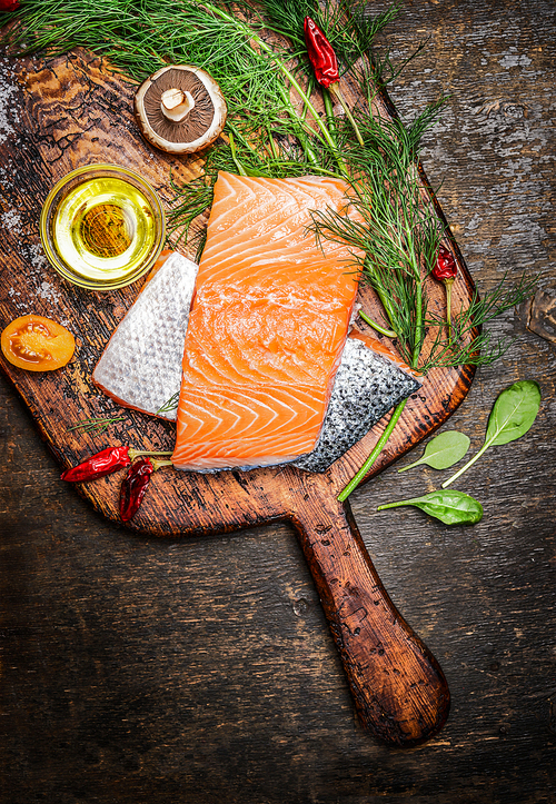 Salmon fillet on old cutting board with oil, herbs and spices, top view, close up