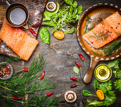 Salmon fillet on rustic kitchen table with fresh ingredients for tasty cooking and frying pan. Wooden background, frame, top view.  Healthy and diet food concept.