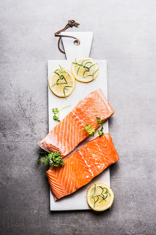 Raw Salmon fish fillet with lemon on white cutting board, top view