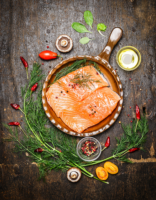 Salmon fillet in fried pan with herbs and ingredients for cooking on rustic wooden background, top view. Healthy food or diet nutrition concept
