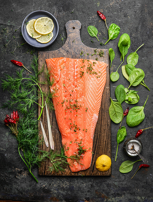 Perfect salmon fillet on rustic cutting board with fresh ingredients for tasty cooking on dark background, top view. Healthy or diet food concept.