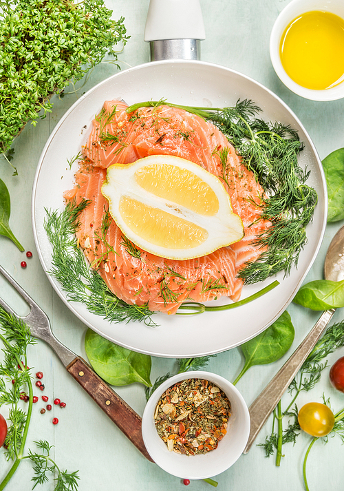 Raw salmon in white pan with lemon, spices, fresh herbs and fork, top view, close up
