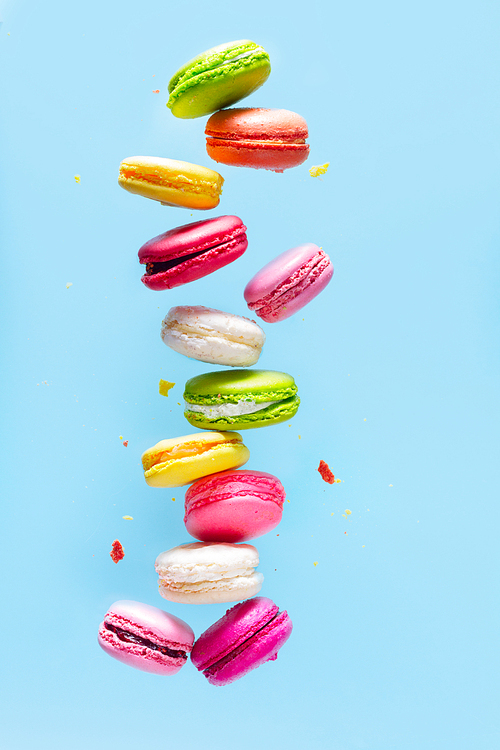 Assorted colorful macaroons falling cookies on blue background