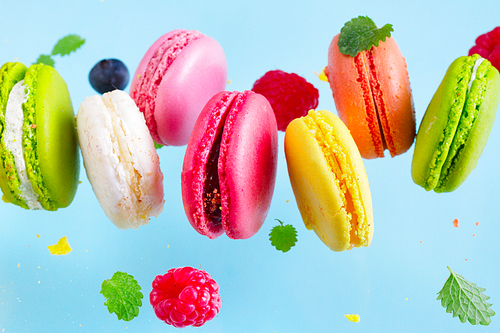 Assorted macaroons falling cookies with berries close up on blue