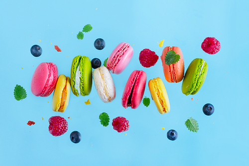 Assorted macaroons falling cookies with berries and leaves on blue background