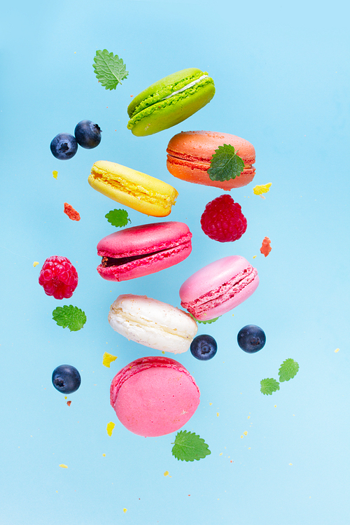 Assorted macaroons falling cookies with berries on blue background