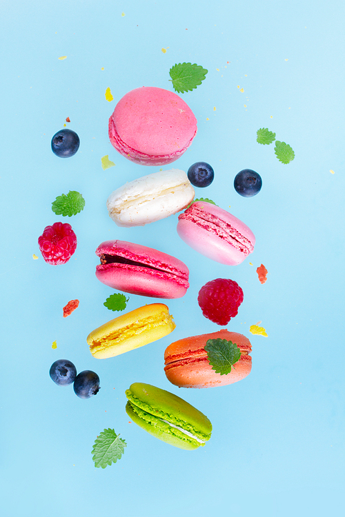 Assorted macaroons falling cookies with berries on blue background