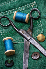 old scissors and thread and buttons on textured background from green jeans