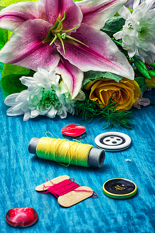 sewing accessories with bouquet of fresh flowers on turquoise background