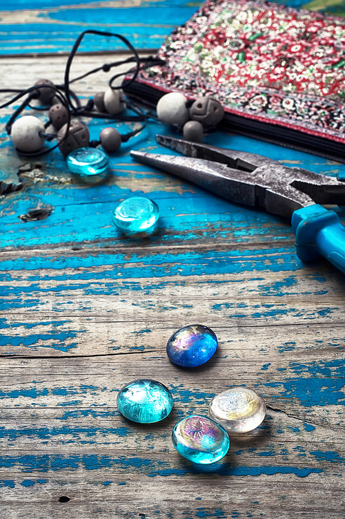 beads,pliers,and other needlework accessories on outdated turquoise wooden background