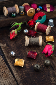 Beads,spools of thread on vintage wooden background decorated with rosebuds
