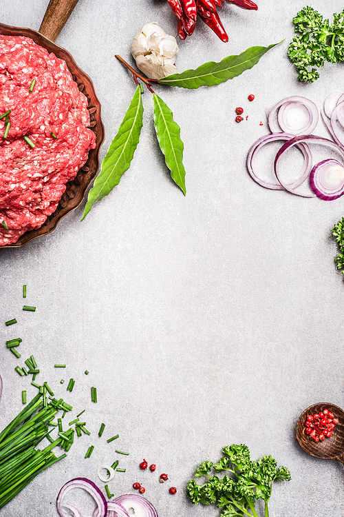 Ground beef with fresh herbs and spices on gray concrete texture background, top view, place for text, frame. Meat food