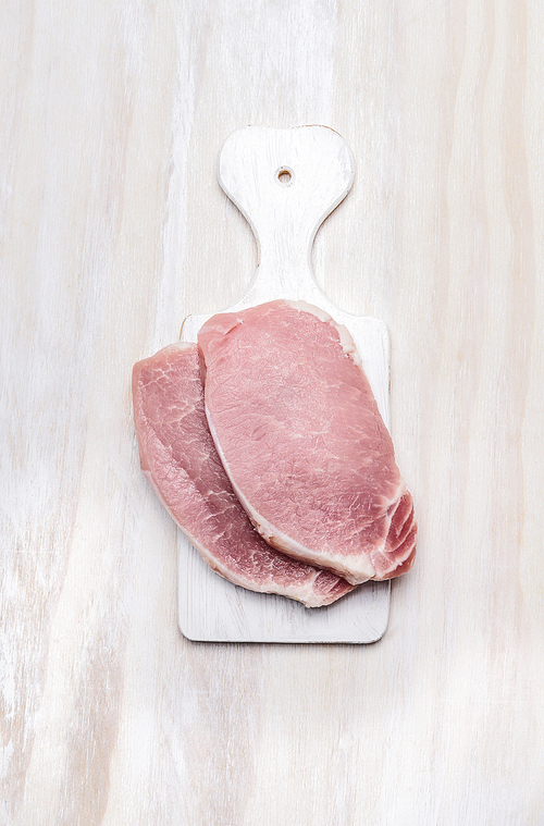 pork loin fillet meat on white cutting board over wooden background, top view