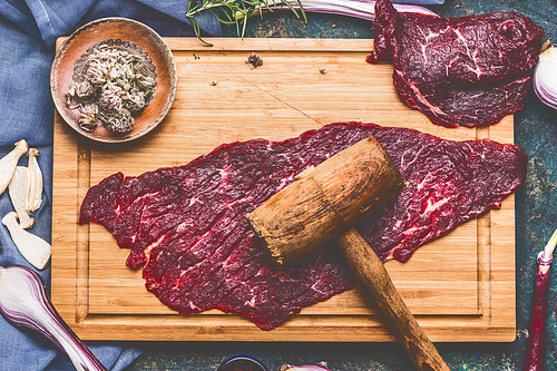 Raw beef chop with wooden meat Tenderizer on cutting board, top view