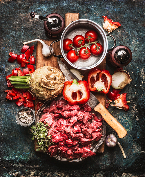 Beef goulash of young bulls with vegetables and cooking ingredients , preparation on cutting  board and dark rustic background , top view composing