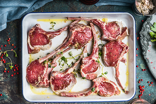 Lamb racks marinating in white enamelled bowl on dark rustic kitchen table, top view