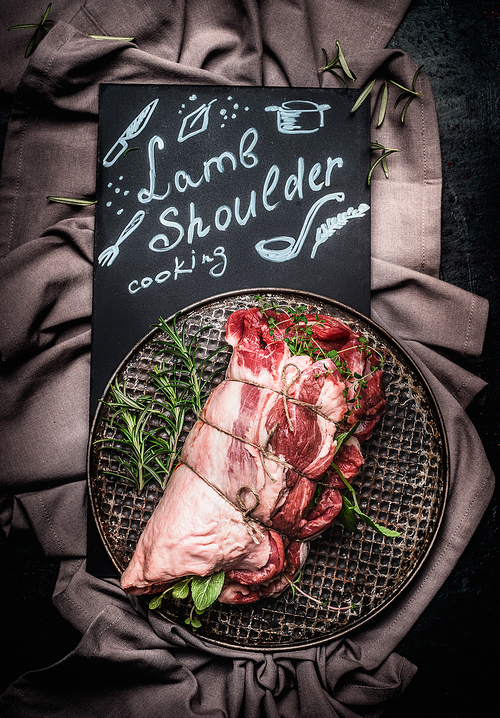 Lettering lamb shoulder cooking on black chalkboard with raw  lamb shoulder roast with string ,  Filled with herbs and spices on vintage baking tray , top view. Meat food.