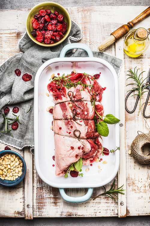 Preparation of Lamb shoulder roast with fresh cooking herbs,spices, Pine nuts and cranberries in casserole on light rustic background, top view