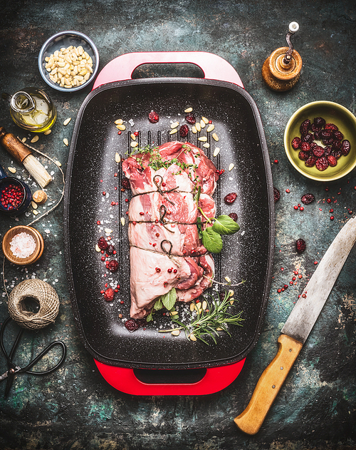 Raw Meat roast preparation in  roaster pan with cooking ingredients and seasoning on dark rustic background with butcher knife, top view