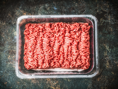 Raw beef minced meat in plastic  box on rustic background, top view, place for text