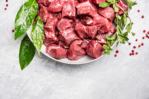 Chopped raw beef meat in white bowl with fresh herbs on light wooden background, top view
