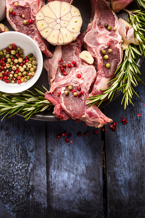 Raw lamb meat with peppercorn, rosemary and garlic on blue rustic wooden table, place for text
