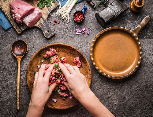 Female hands making minced meat stuffing on kitchen table background with  meat, force meat , meat grinder and spoon, top view. Cooking,recipes and eating concept